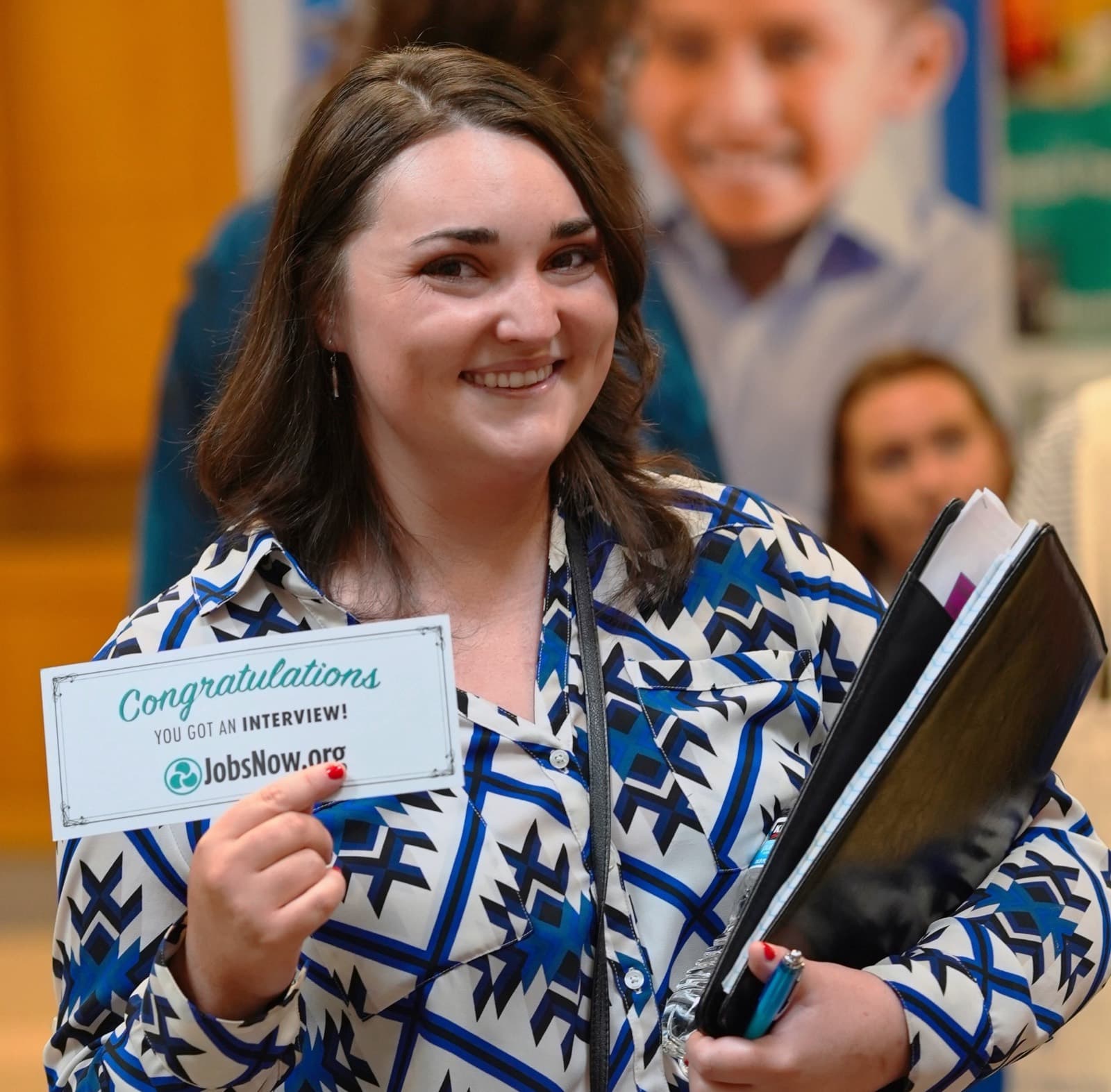 A job seeker at a JobsNow.org job fair holding a card that reads “Congratulations, you got an interview!”
